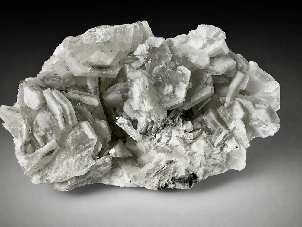 Open cluster of white and pale grey tabular poker chip Calcite on grey stone matrix from Liancheng, China